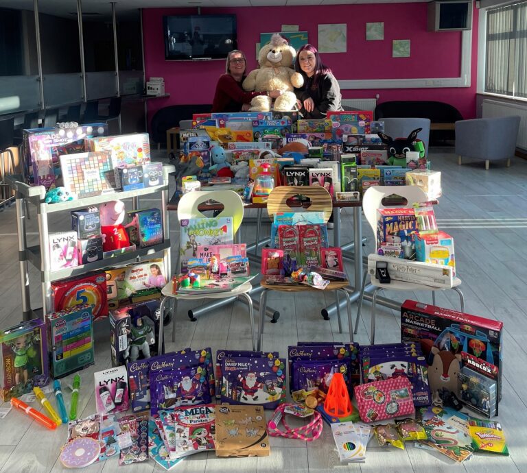 Two people pose with Christmas presents that have been donated for a charity campaign.